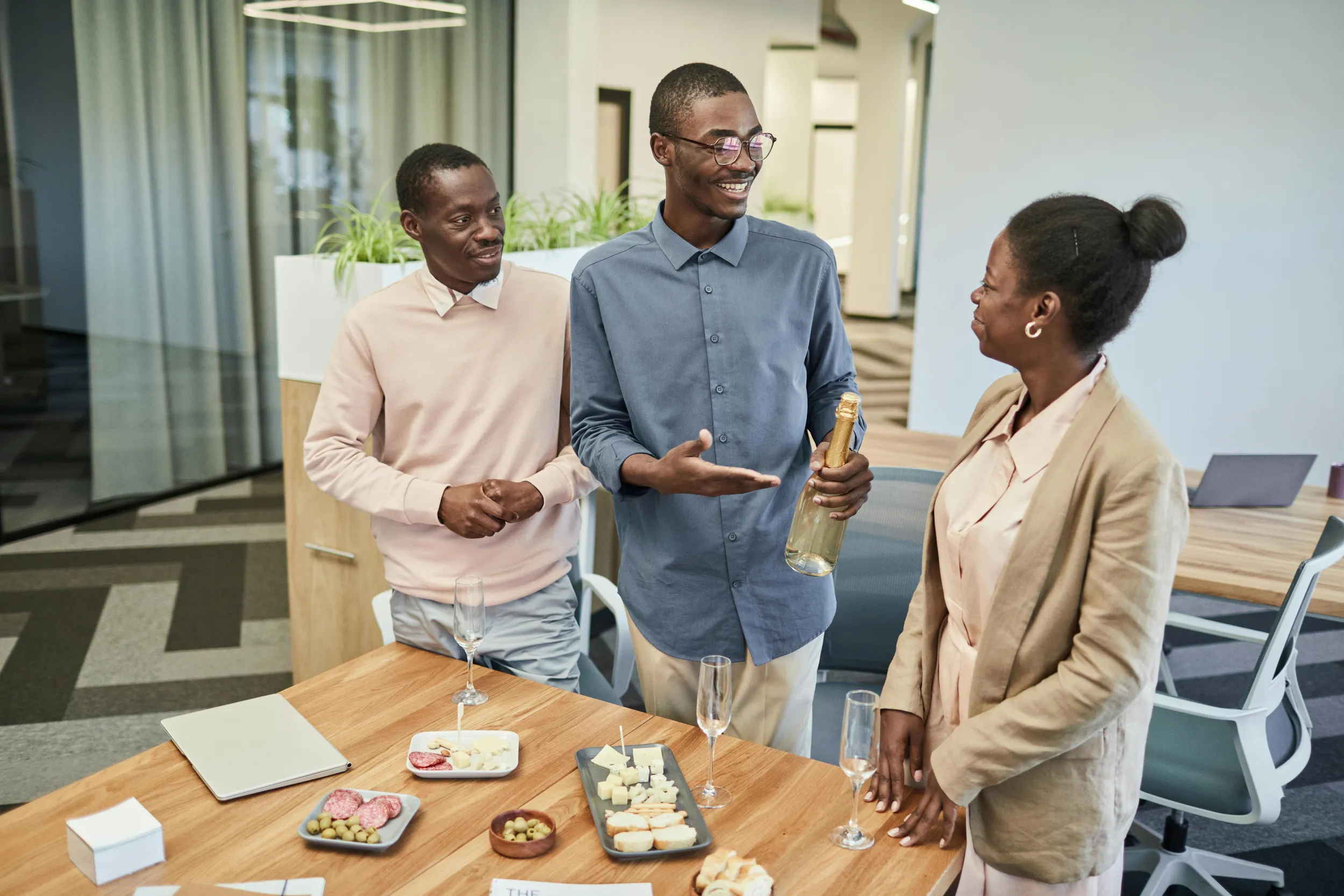 Collega met een fles bubbels wijst lachend naar jubilaris tijdens werkjubileumviering.