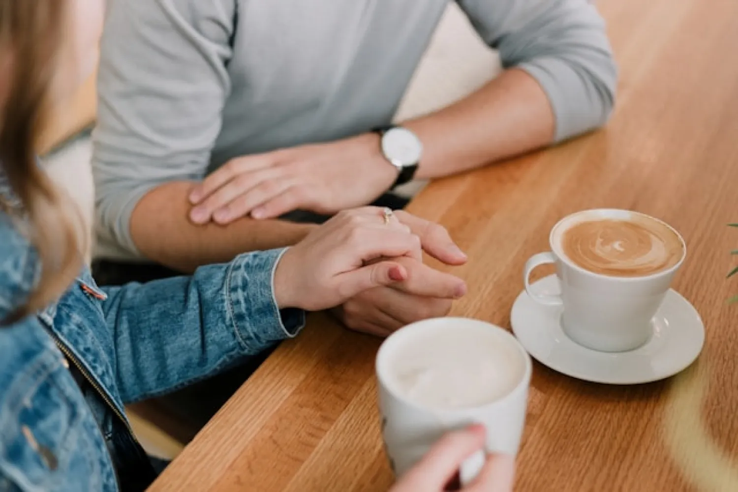 Twee mensen die elkaars handen vasthouden aan een tafel, passend bij een relatie op de werkvloer