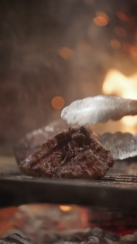 Stuk vlees wordt met een tang gedraaid op een grill.