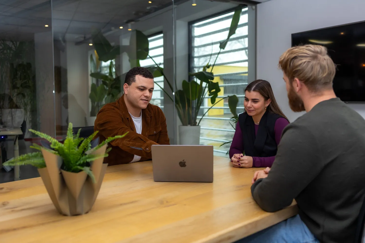 Twee mannen en een vrouw kijken gezamenlijk naar een laptop
